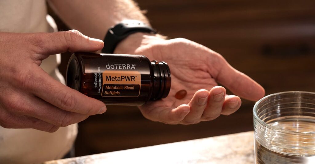 Hand holding MetaPWR metabolic blend softgels next to a glass of water.