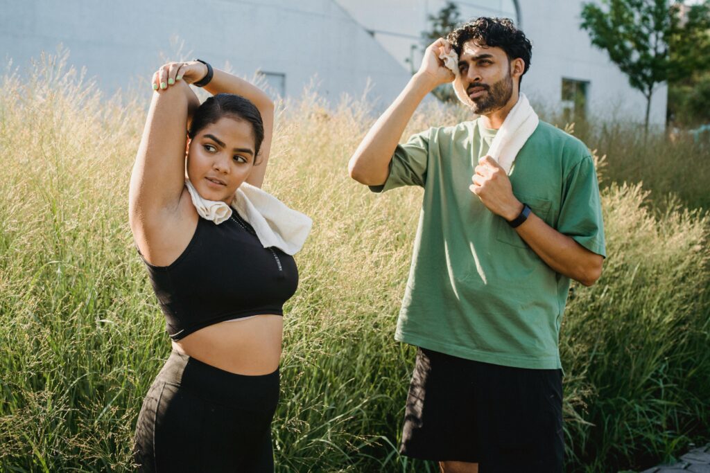 Pair stretching outdoors with towels around necks; fitness and health focus.